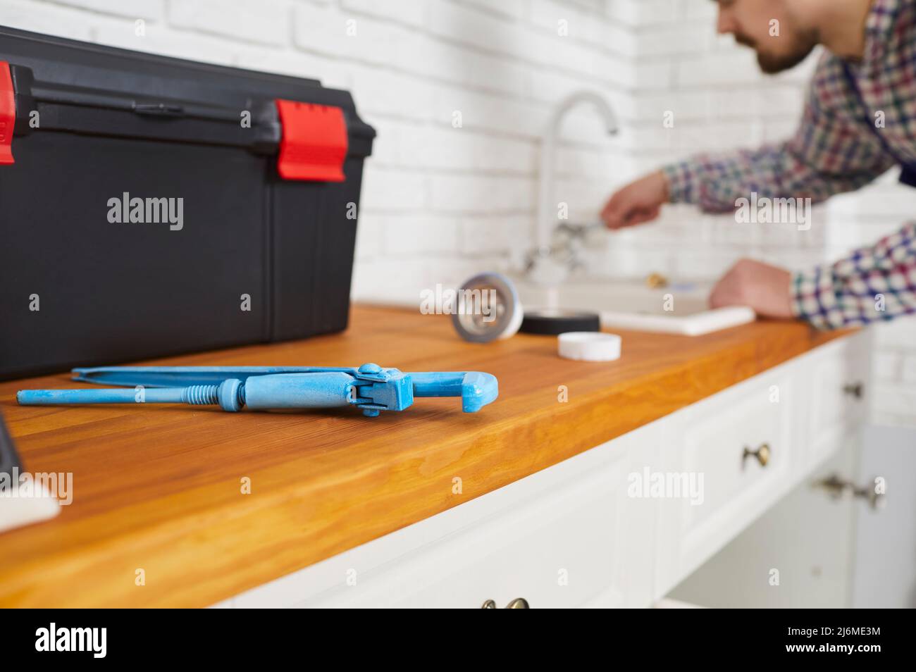 Idraulico usando una chiave e altri attrezzi mentre ripara il rubinetto del dispersore nella cucina Foto Stock