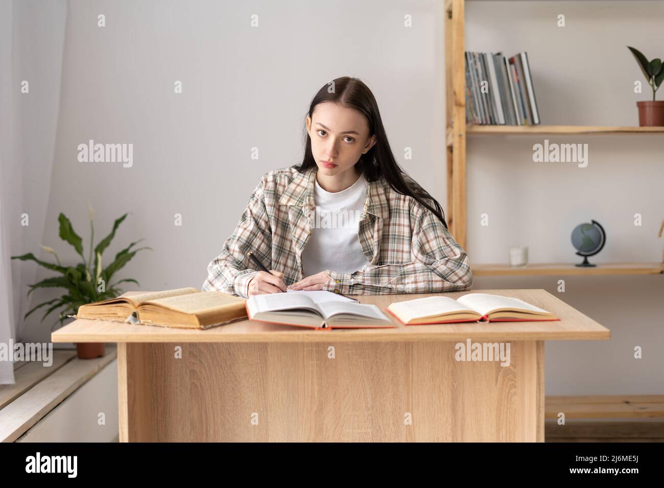 Studente di scuola superiore che prende appunti da un libro per lo studio. Ragazza caucasica seduta al tavolo facendo i compiti. Ragazza focalizzata che studia in classe Foto Stock