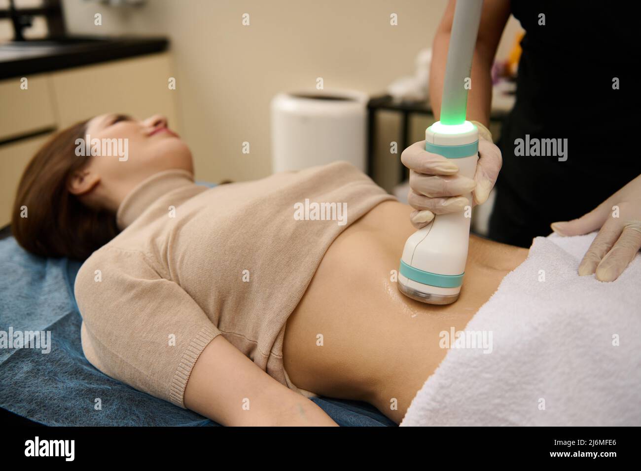 Concentratevi su un trasduttore a ultrasuoni touch che si sposta sopra il contatto gel lubrificato pancia di giovane donna in forma corpo che riceve la terapia di cavitazione in spa cl Foto Stock
