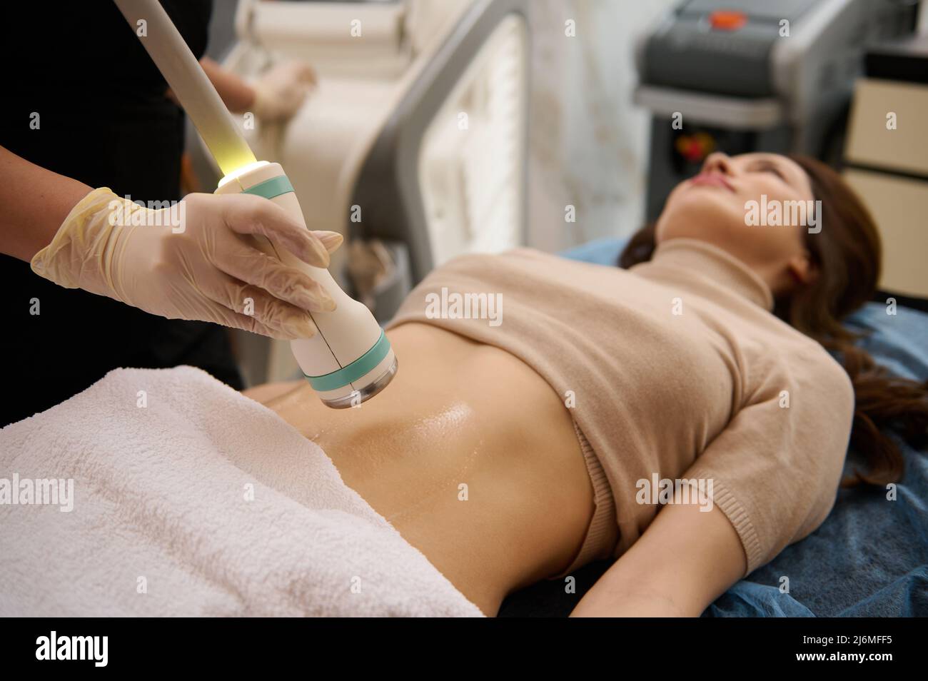 Concentratevi su un trasduttore a ultrasuoni touch che si sposta sopra il contatto gel lubrificato pancia di donna sfocata ottenere corpo plasmare la terapia di cavitazione in clinica spa Foto Stock