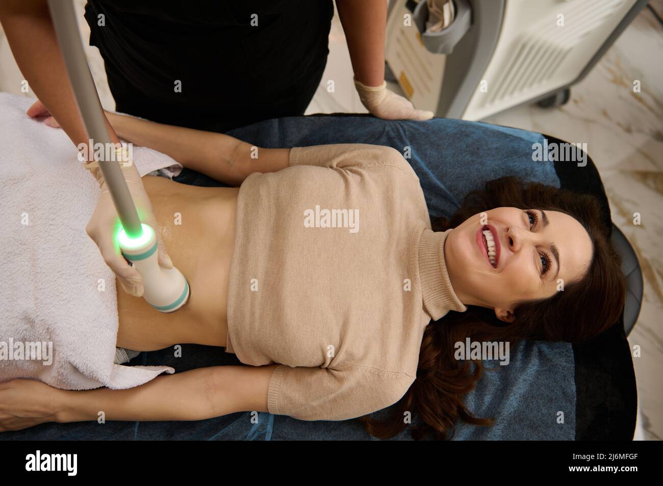 Vista dall'alto di una giovane donna che riceve la microstimolazione dei muscoli addominali, con uno speciale sensore di cavitazione a radiofrequenza in una clinica termale. Tempra Foto Stock