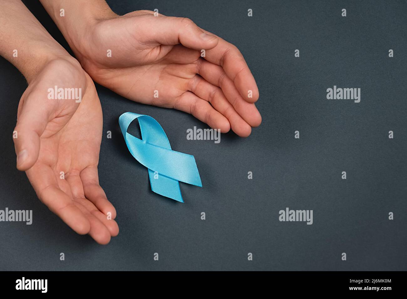 Primo piano delle mani maschili e nastro blu sulla parete grigia dello studio. Consapevolezza del cancro della prostata, consapevolezza di salute degli uomini di Movember. Sanità, interno Foto Stock