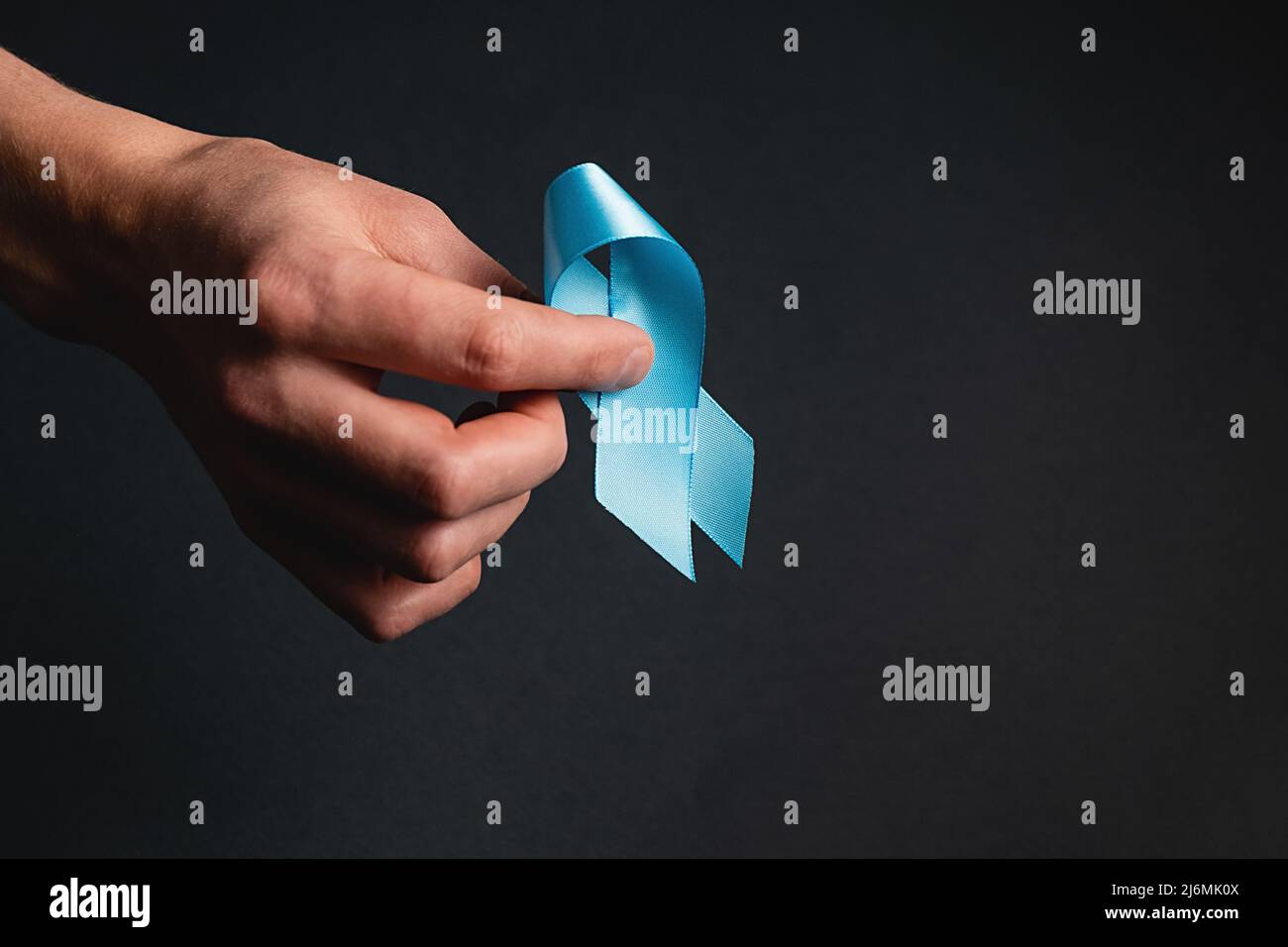Primo piano della mano maschio che tiene il nastro blu sulla parete di fondo grigio scuro. Consapevolezza del cancro della prostata, consapevolezza di salute degli uomini di Movember. Sanità, interno Foto Stock