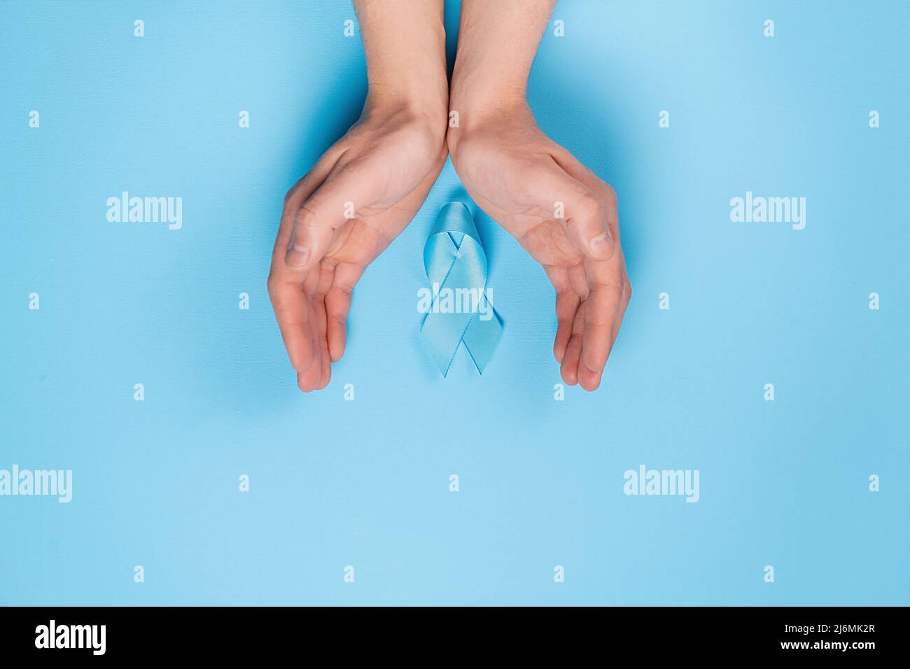Primo piano delle mani maschili e nastro blu sulla parete blu dello studio. Consapevolezza del cancro della prostata, consapevolezza di salute degli uomini di Movember. Sanità, interno Foto Stock