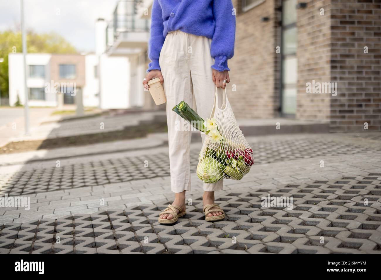 Donna con sacco a rete pieno di verdure e tazza di caffè riutilizzabile all'aperto Foto Stock
