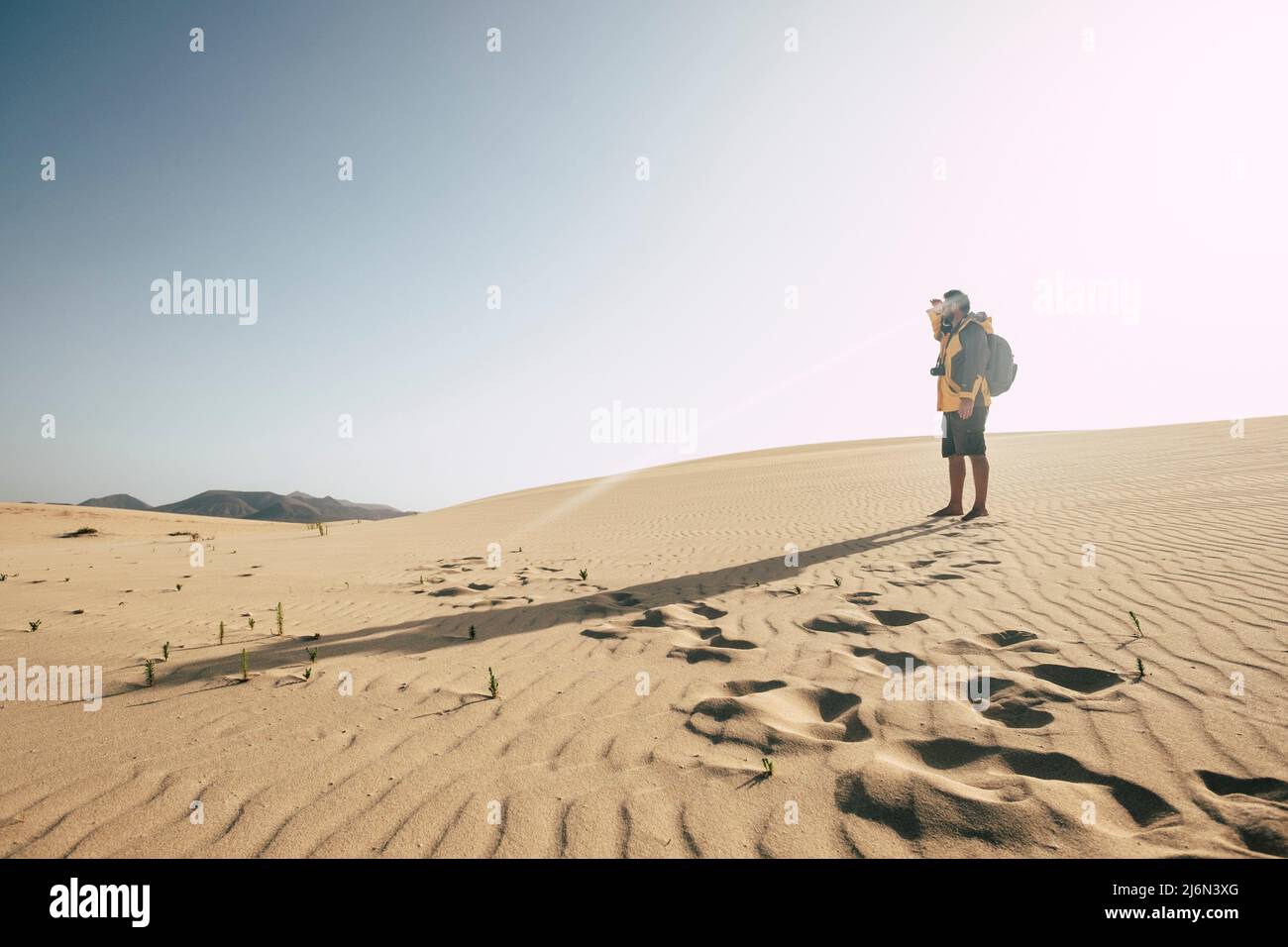 Un uomo in piedi sulle dune del deserto di sabbia con zaino guardando lontano - cambiamento climatico arido non acqua futuro mondo terra concetto - alternative selvaggio Foto Stock
