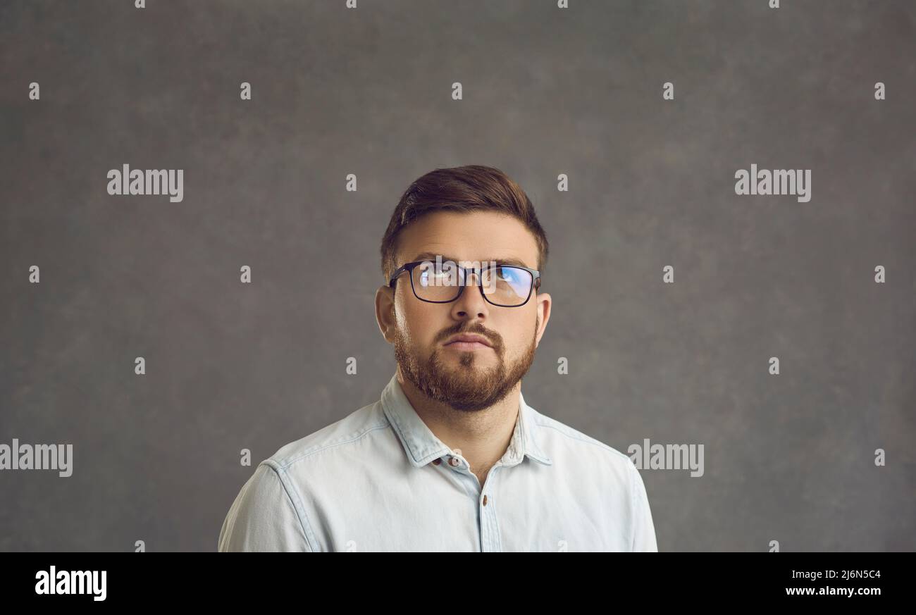 Uomo serio in occhiali guardando su a qualcosa di sospetto e pensando che cosa fare a questo proposito Foto Stock