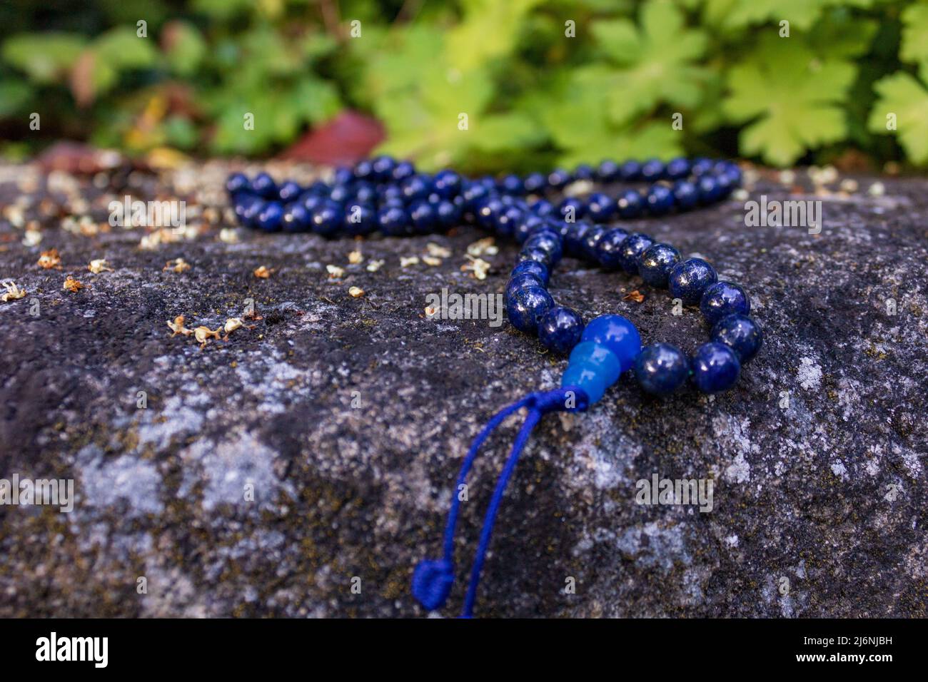 Primo piano di perle di preghiera buddista blu su pietra su sfondo verde. Mala perline per la consapevolezza e la meditazione. Foto Stock