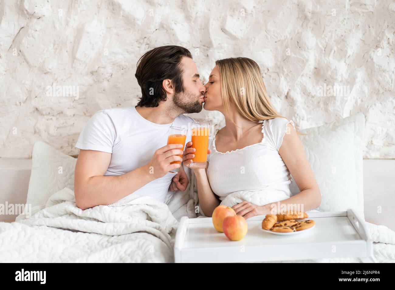 Una giovane coppia che ama fare colazione a letto insieme, baciare, trascorrere la luna di miele in hotel Foto Stock