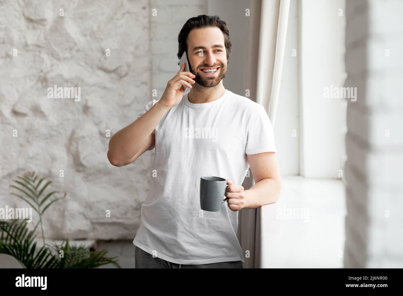 Uomo ben riposato che fa una telefonata mentre beve il caffè Foto Stock