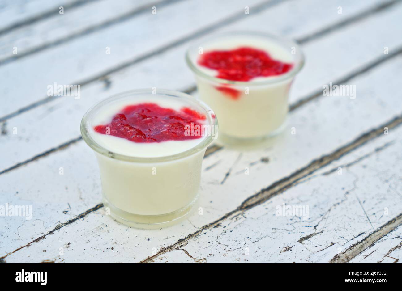 Sano yogurt semplice fatto in casa in una piccola tazza di vetro, condimento con marmellata di fragole organiche, la tazza di yogurt sono su tavola di legno bianco rustico. Foto Stock