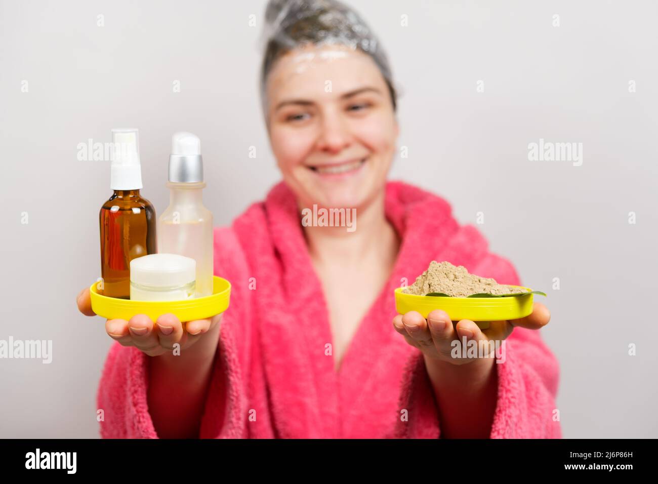 Una donna con un film sulla testa fa una maschera per capelli e tiene in mano cosmetici naturali e innaturali Foto Stock