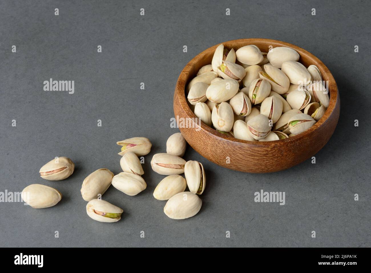 Pistacchi verdi in ciotola di legno su fondo di cemento scuro. Spazio di copia per il testo. Snack sano alle noci. Foto Stock