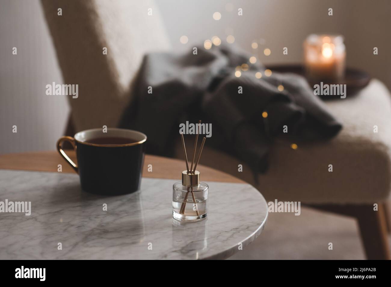 Bastoncini di bambù in bottiglia con candele profumate e una tazza di tè sul primo piano del tavolo di marmo. Aroma domestico. Aromaterapia. Soggiorno in appartamento. Foto Stock