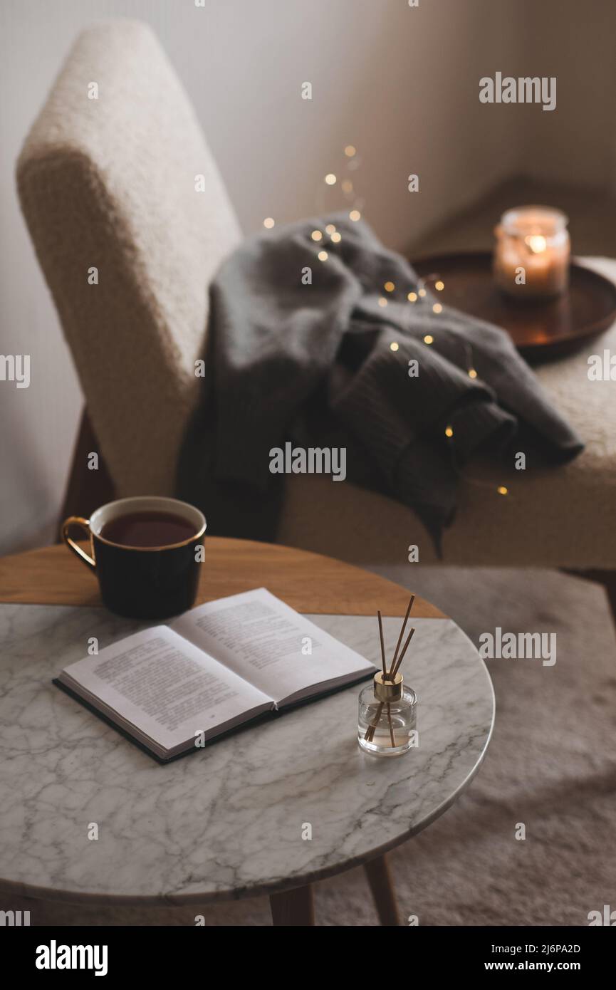 Bastoncini di bambù in bottiglia con candele profumate con tazza di tè e libro aperto sul primo piano del tavolo di marmo. Aroma domestico. Aromaterapia. Soggiorno in appartamento. Foto Stock