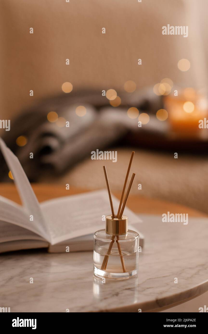 Bastoncini di bambù in bottiglia con candele profumate e libro aperto sul primo piano del tavolo di marmo. Aroma domestico. Aromaterapia. Soggiorno in appartamento. Foto Stock