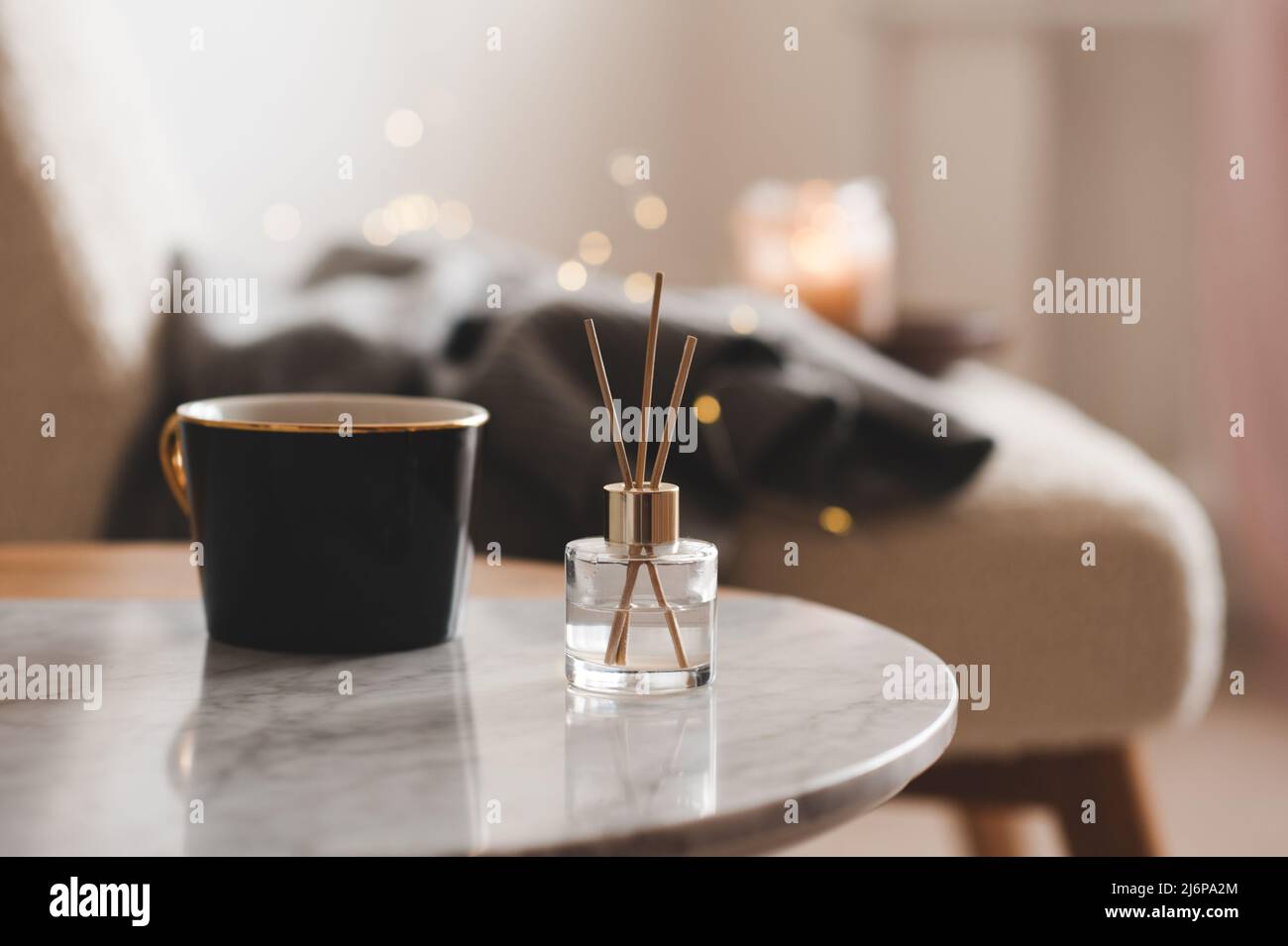 Bastoncini di bambù in bottiglia con candele profumate e una tazza di tè sul primo piano del tavolo di marmo. Aroma domestico. Aromaterapia. Soggiorno in appartamento. Foto Stock