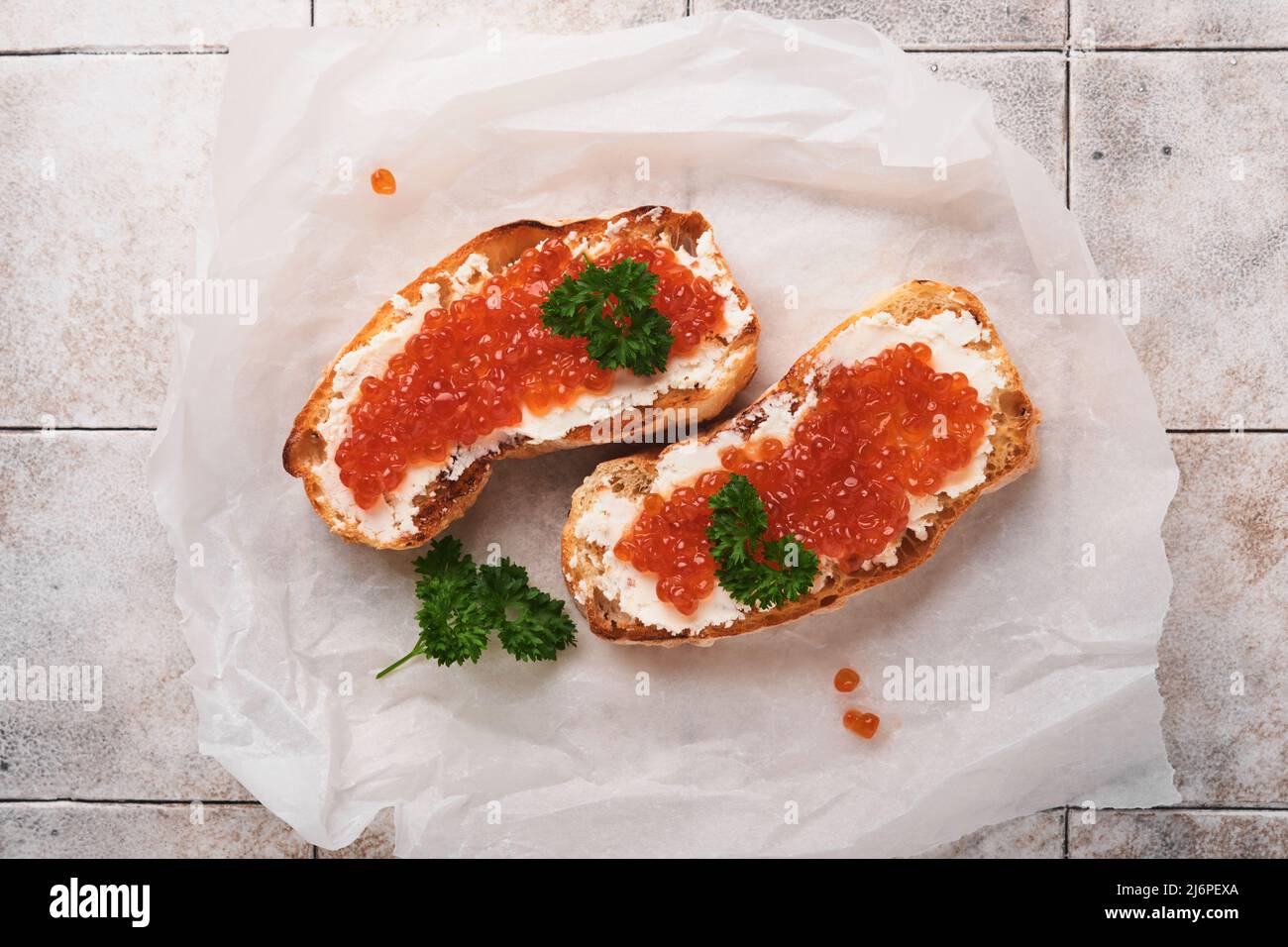 Due dandwiches con caviale rosso. Caviale rosso salmone in ciotola e sandwich server su carta pergamena su vecchio sfondo grigio cracked tabella piastrelle. Vista dall'alto Foto Stock