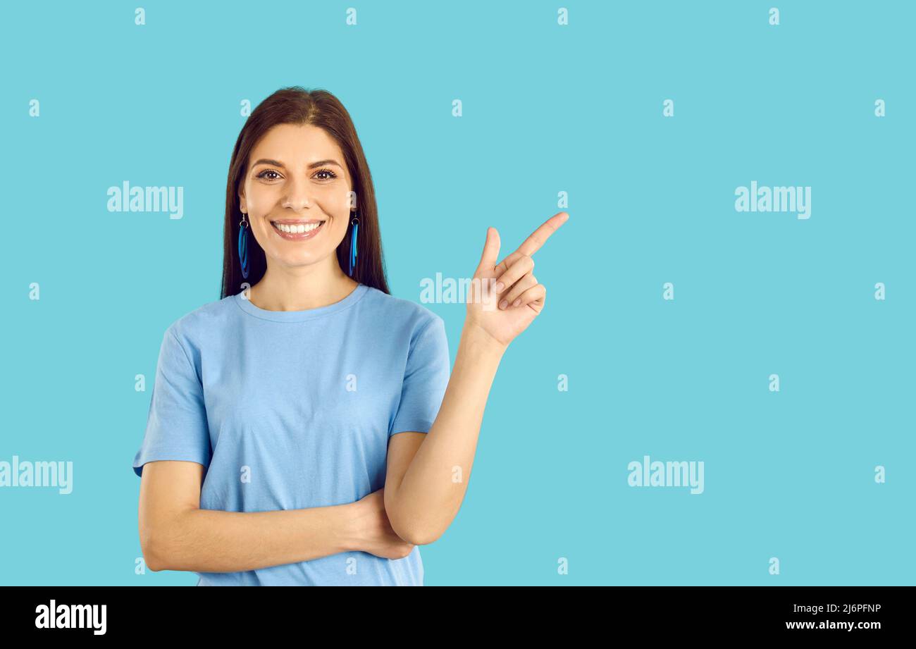 Felice bella donna che punta con il suo dito a qualcosa su sfondo blu spazio copia Foto Stock