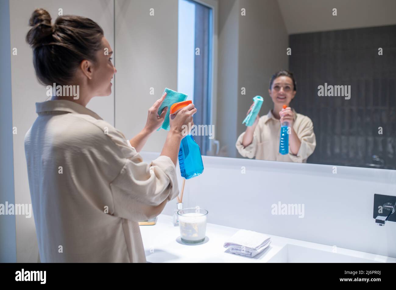 Giovane donna con ciocca in piedi vicino allo specchio in bagno Foto Stock