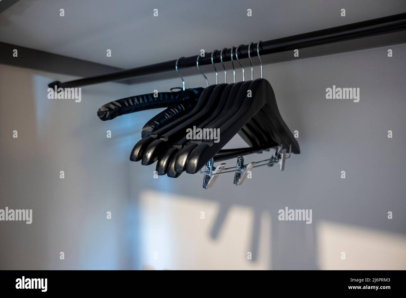 Vista ad angolo di grucce in legno nero con clip all'interno di un pulito armadio bianco della camera d'albergo Foto Stock