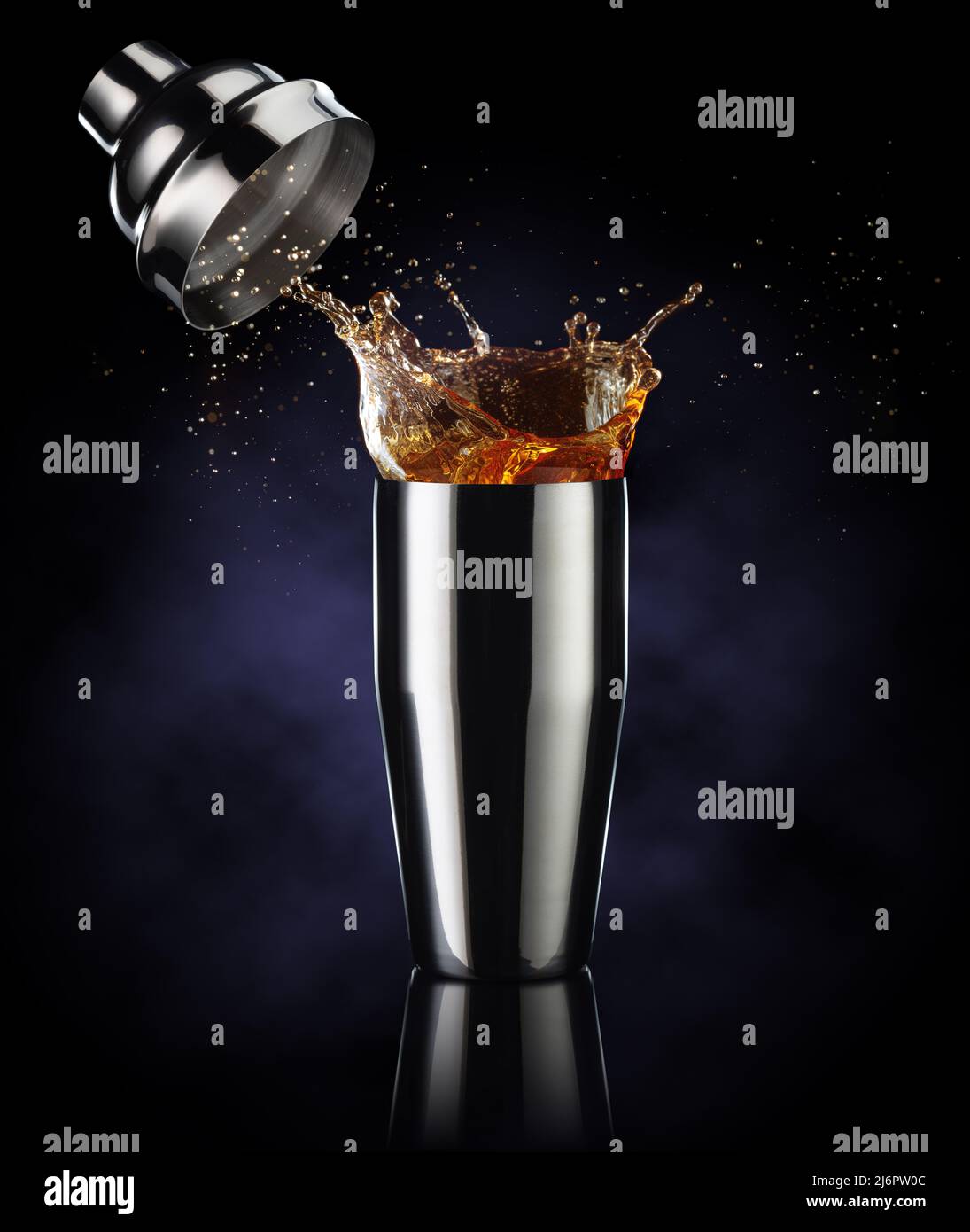 liquido ambrato fuoriuscito da uno shaker isolato su sfondo blu scuro Foto Stock