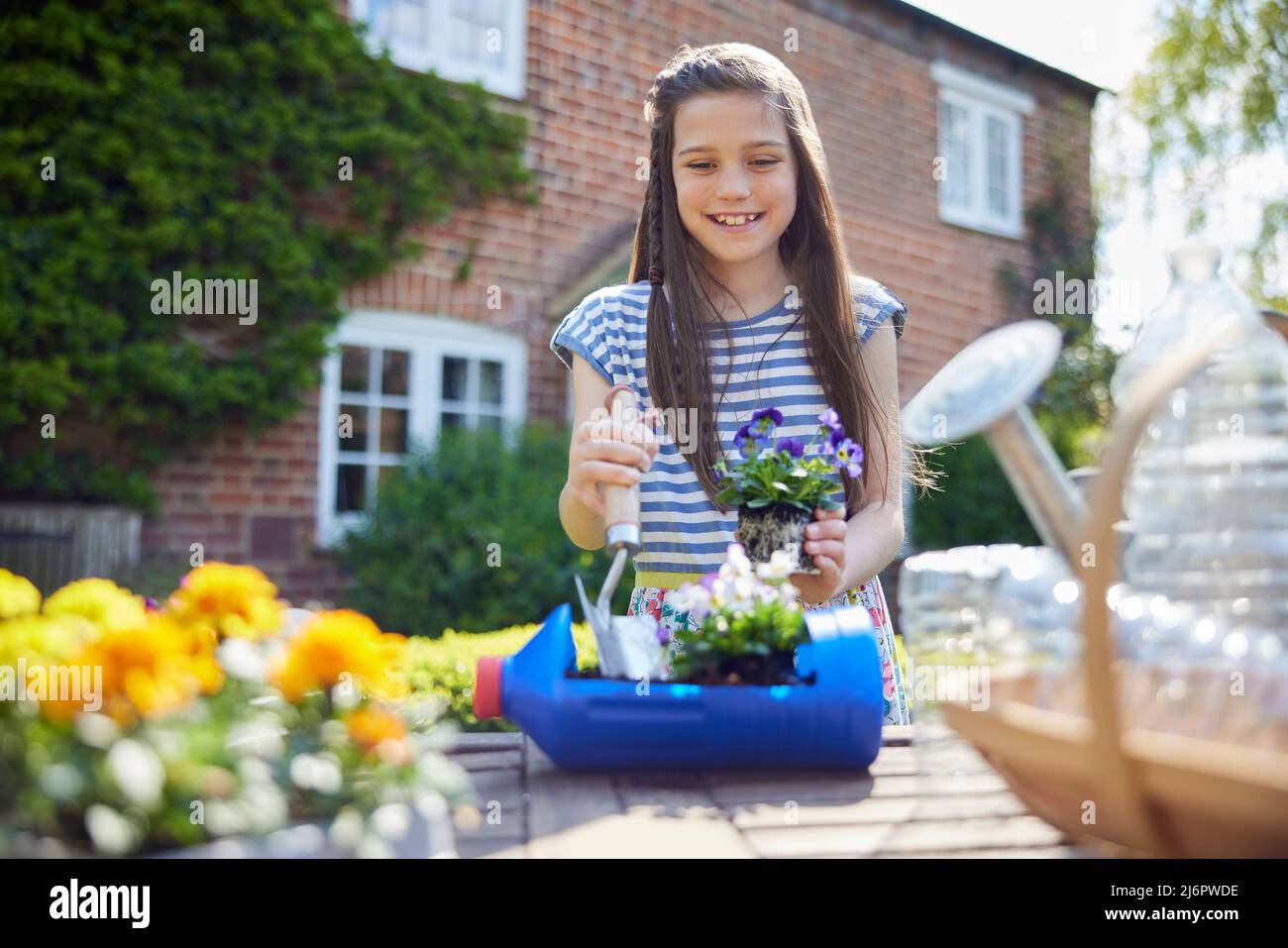 Sorridente ragazza che fa il supporto di pianta riciclato dalla bottiglia di plastica rifiuti di imballaggio in giardino a casa Foto Stock