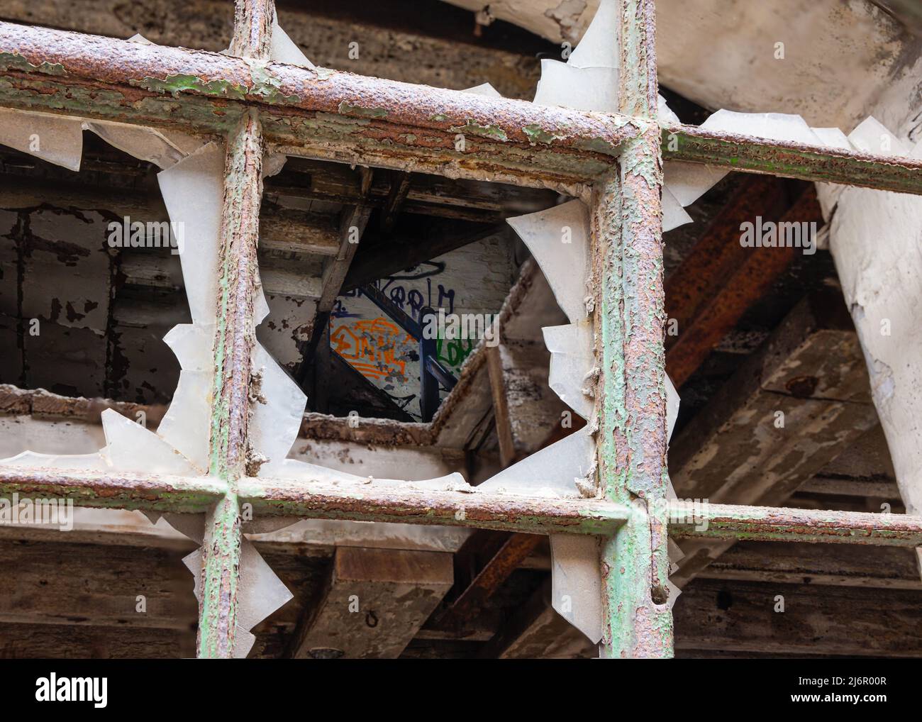 Lastre di vetro rotte in cornici quadrate di metallo, ricoperte di ruggine e vernice verde peeling. Un interno derelitto è visibile oltre. Foto Stock
