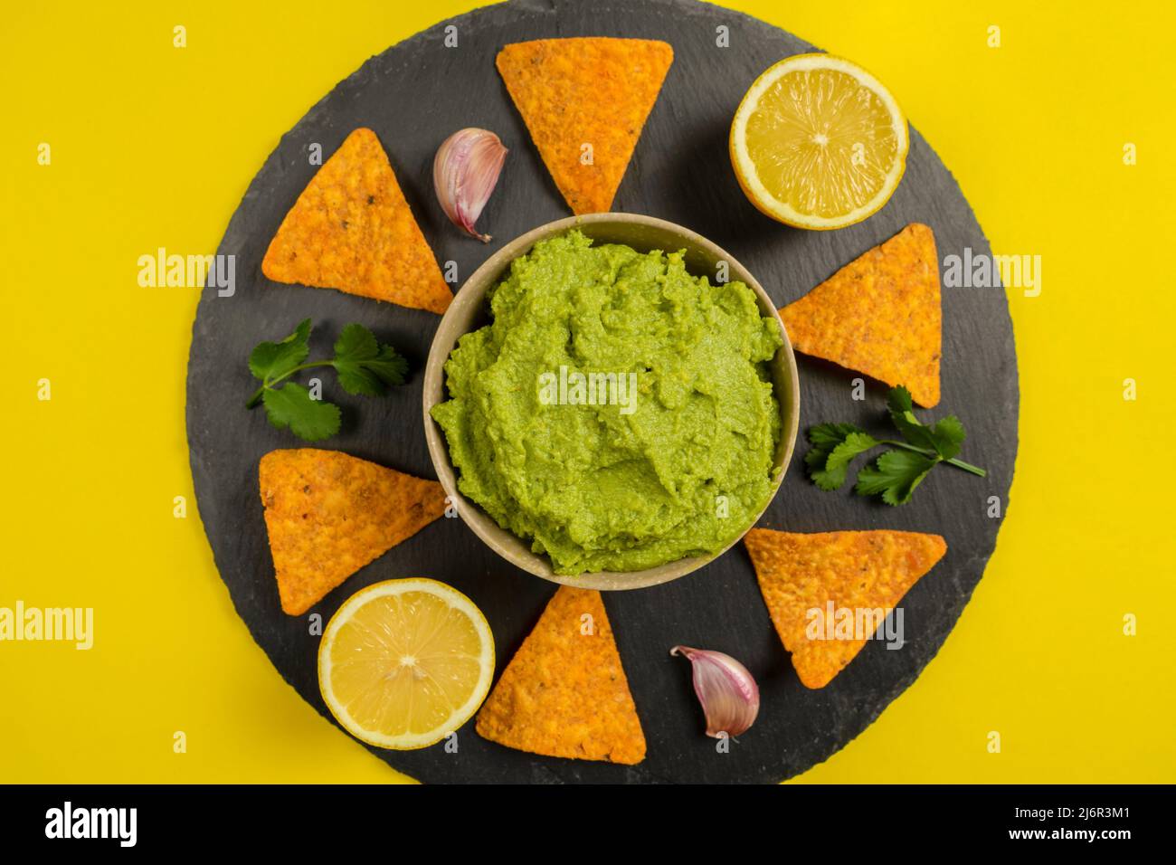 Composizione di guacamole con gli ingredienti per la sua creazione e il nachos per il suo consumo su sfondo giallo. Foto Stock