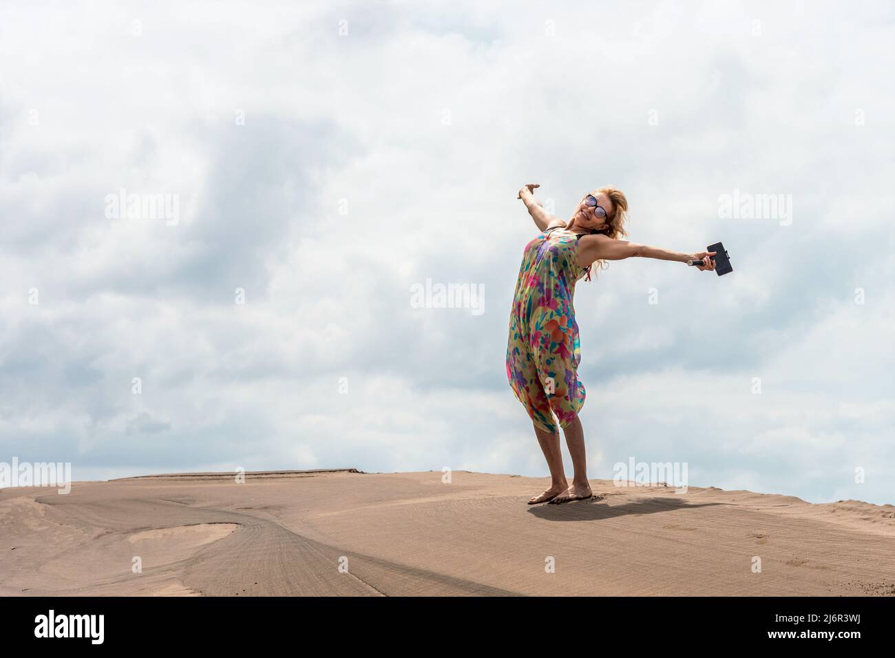 Donna sorridente bionda che gestura la felicità sulla cima di una duna di sabbia Foto Stock