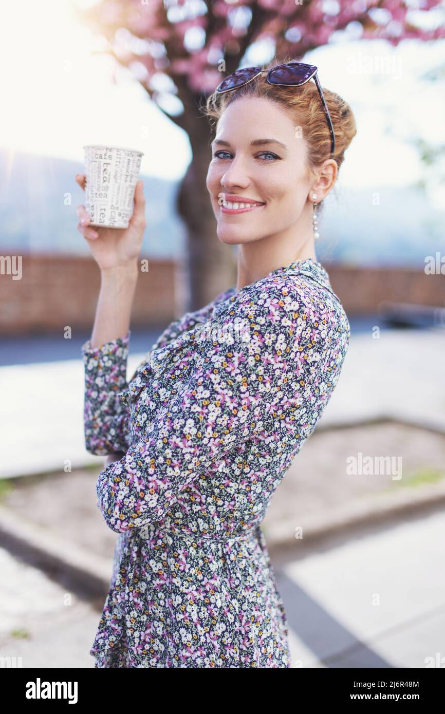 Giovane donna rossa fresca con un sorriso toothy che tiene una tazza di caffè di plastica all'aperto Foto Stock