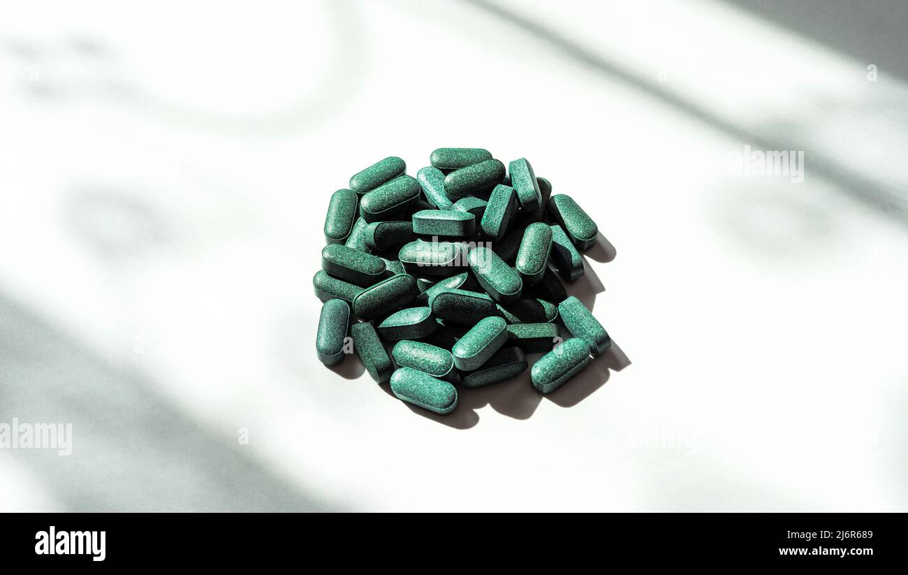 Pillole di clorella, spirulina, erba d'orzo su sfondo bianco con ombre scure primo piano e ombra modello nutrizionale supplemento, detox superfood Foto Stock