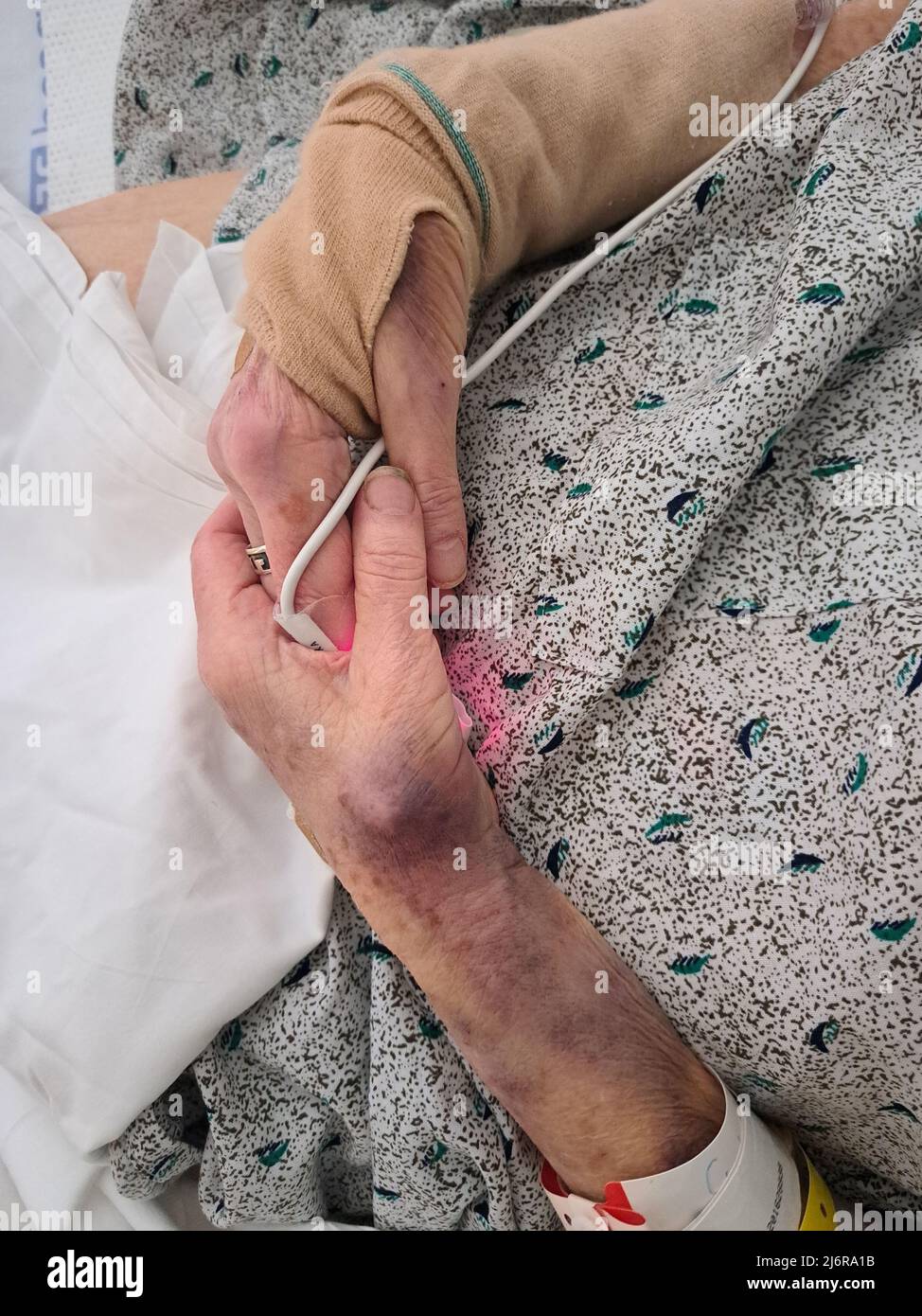 La donna anziana stringe le mani sopra la cammetta dell'ospedale. Foto Stock