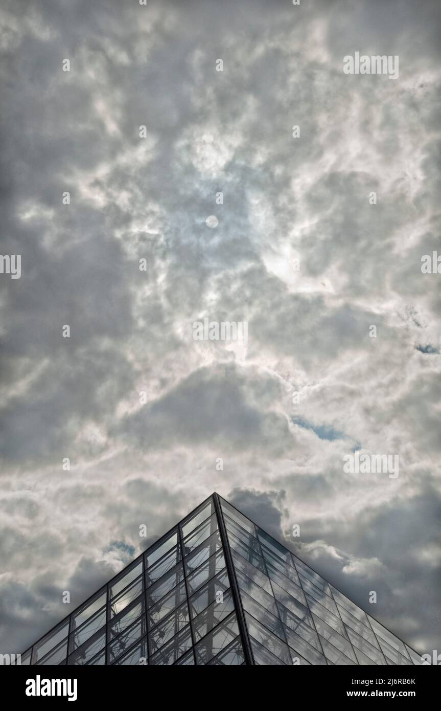 Il sole che oscilla dietro le nuvole galleggia dietro l'ingresso principale del musée du Louvre. Foto Stock