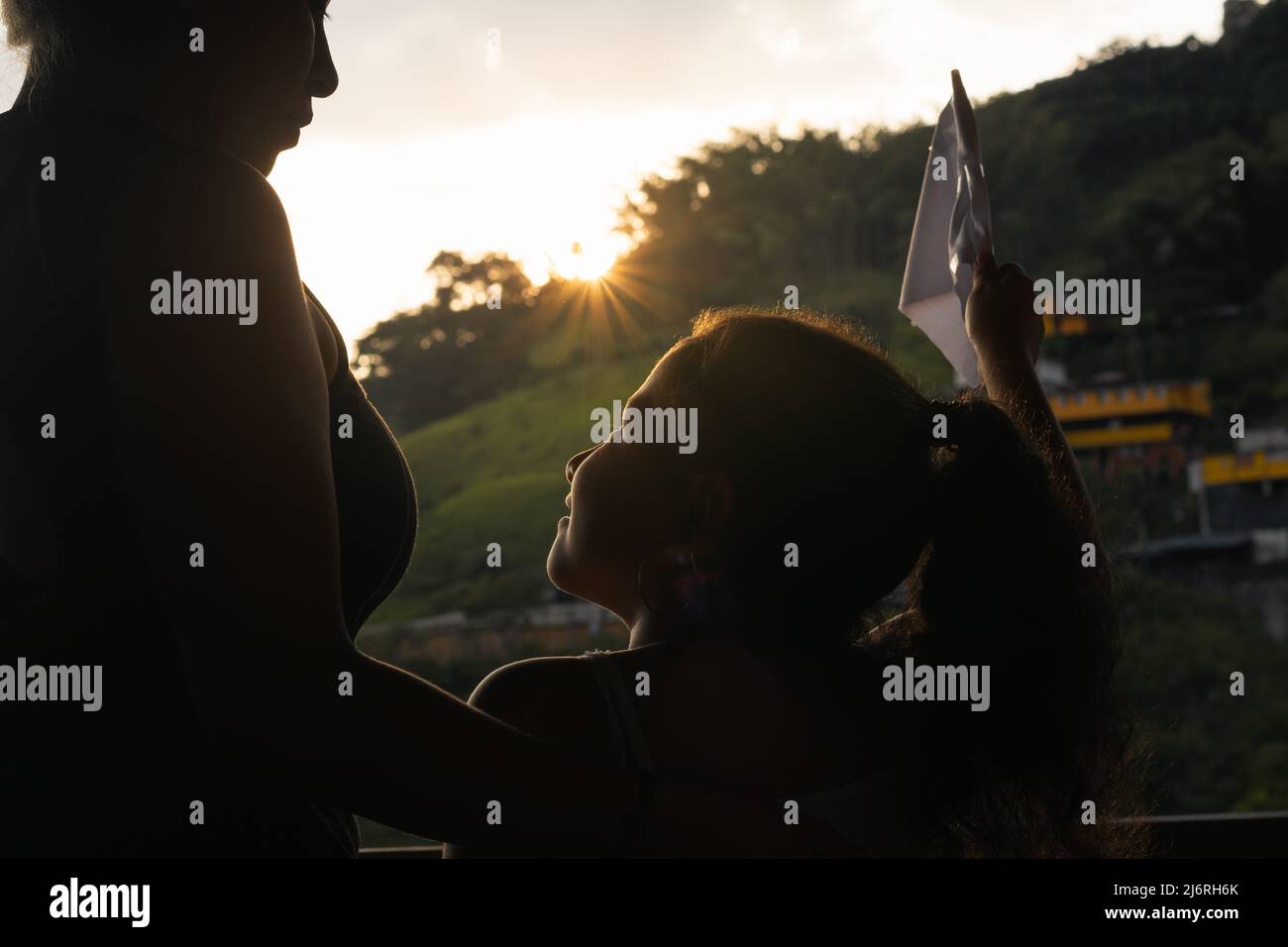 Silhouette di una giovane madre con sua figlia, sullo sfondo un bel tramonto nascosto dietro le belle montagne colombiane. Ragazza che tiene una w Foto Stock