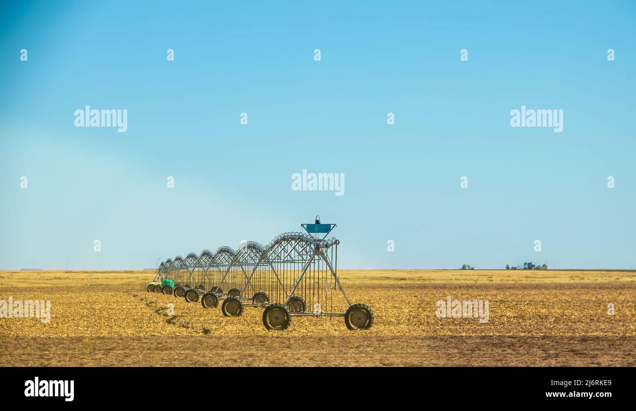 Sistema di irrigazione su ruote che si trovano in un terreno agricolo piano e marrone sotto il cielo azzurro Foto Stock