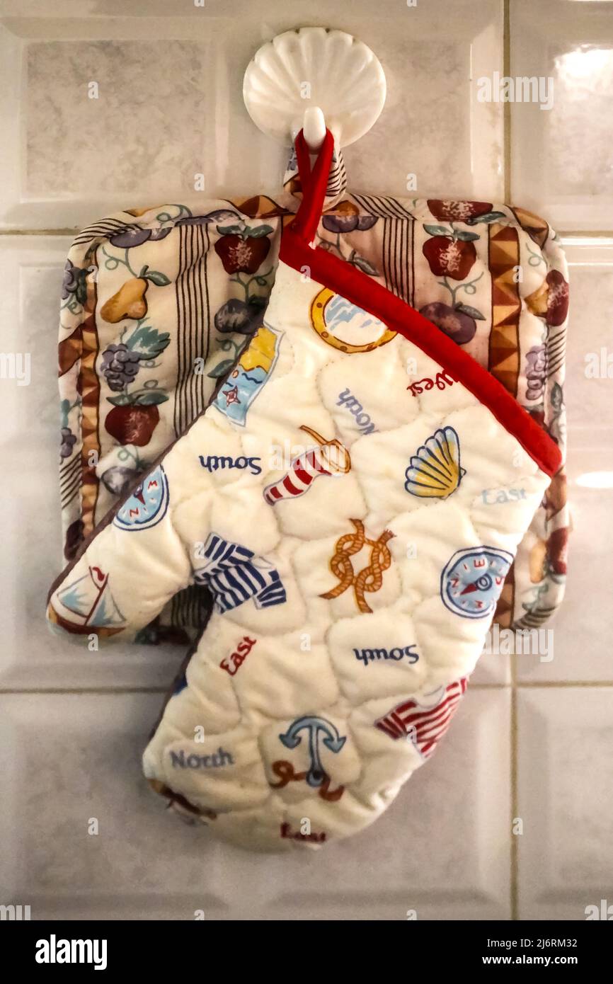 Moms cucina - un potholder ed un mitt del forno appendono da un appendiabiti a forma di guscio di plastica sulla piastrella in una cucina casalinga - primo piano Foto Stock