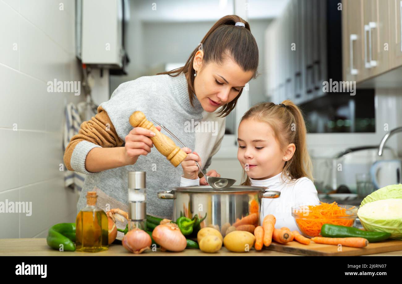 La figlia che aiuta a cucinare la zuppa e la madre aggiungono il pepe alla padella Foto Stock