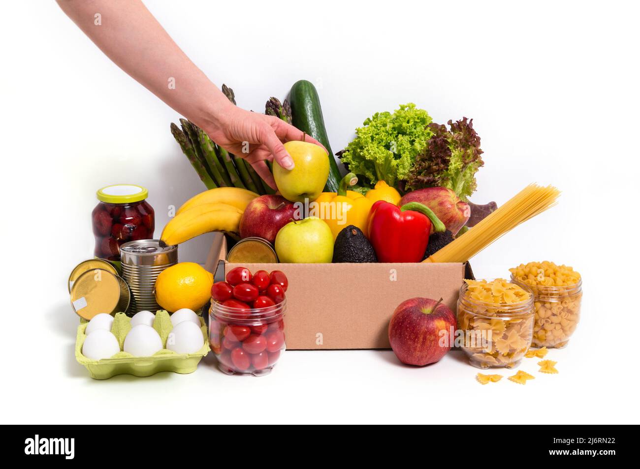 Mettere a mano o prendere la mela dalla scatola con frutta fresca e verdure, uova, pasta e cibi in scatola. Concetto di donazione o consegna di cibo. Vegetariano Foto Stock