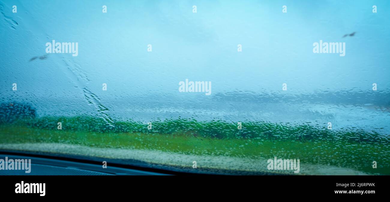 Vista attraverso il finestrino dell'auto schermo distorto e sfocato con caduta di pioggia gocce fuori sopra il bordo erboso della scogliera a mare tempestoso e gabbiano. Foto Stock