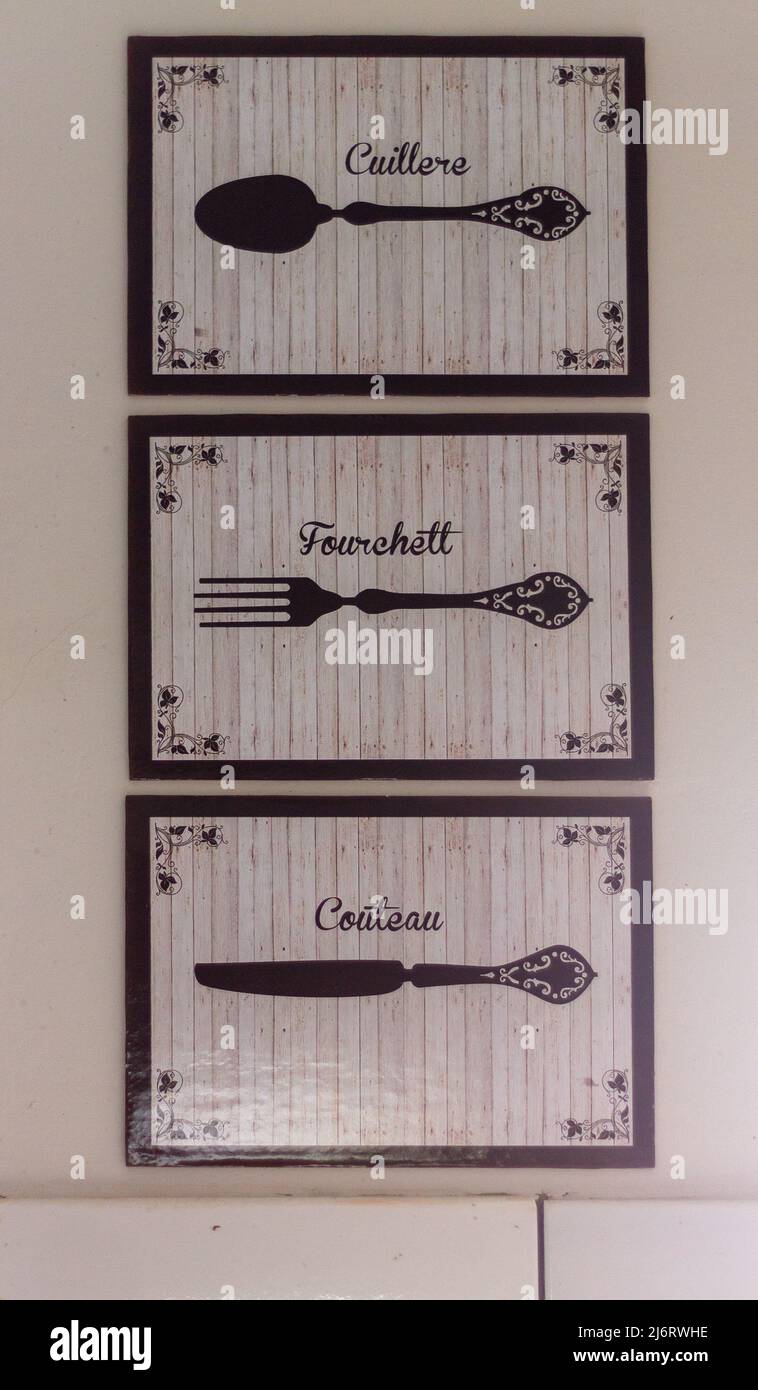 tre dipinti color crema e nero con disegni di forchetta, coltello e cucchiaio, con le descrizioni scritte in francese sul muro di una cucina Foto Stock