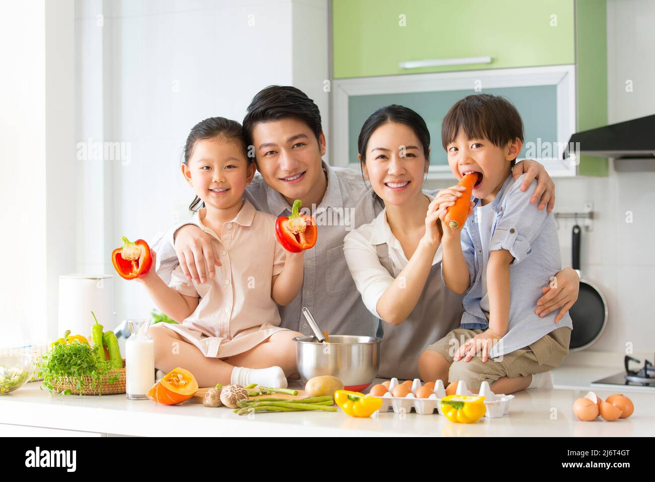 Famiglia cucina parentage. I giovani genitori giocano con due preschoolers, che si siedono sul banco della cucina che mostra le verdure. - foto di scorta Foto Stock