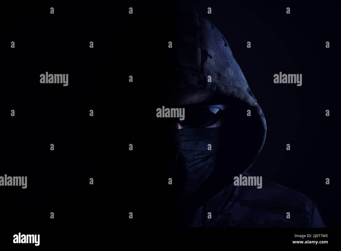 Uomo elegante con cappuccio scuro con occhiali neri e maschera sfondo scuro, hacker, attaccante e bandito Foto Stock
