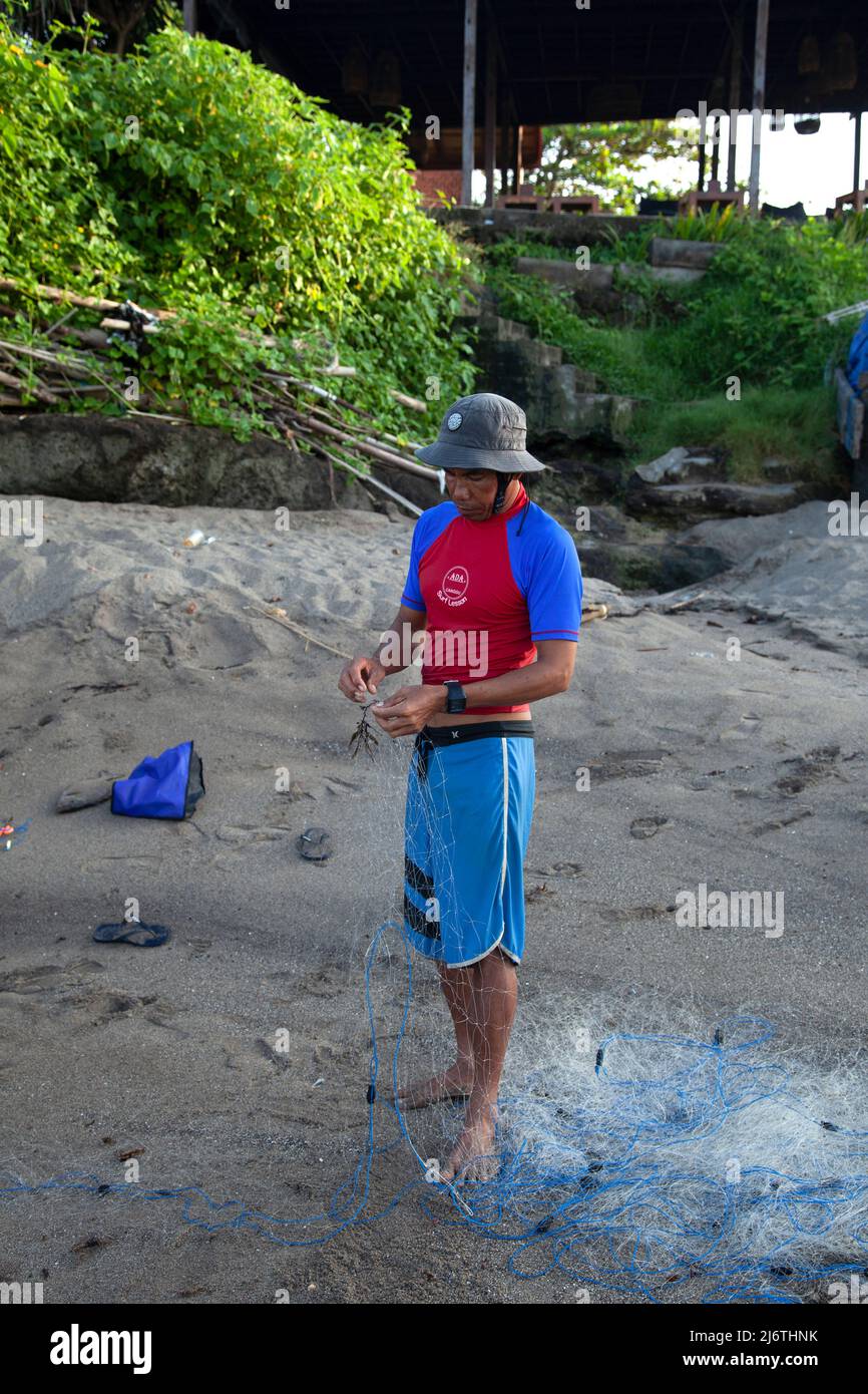 Pescatore che ripara la rete a Batu Bolong Beach a Canggu, Bali, Indonesia Foto Stock