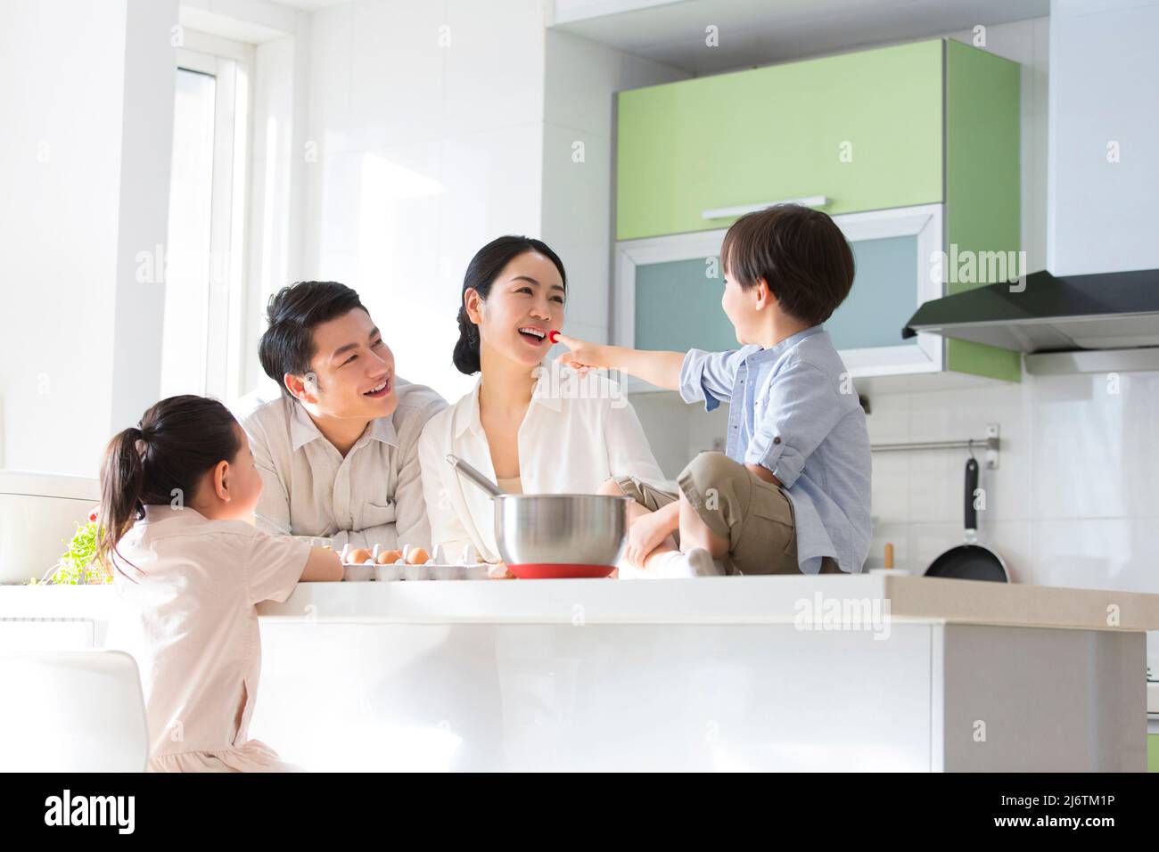 Famiglia cucina parentage. Una famiglia di quattro cuochi insieme in cucina, mentre il figlio spinge un lampone alla madre. - foto di scorta Foto Stock