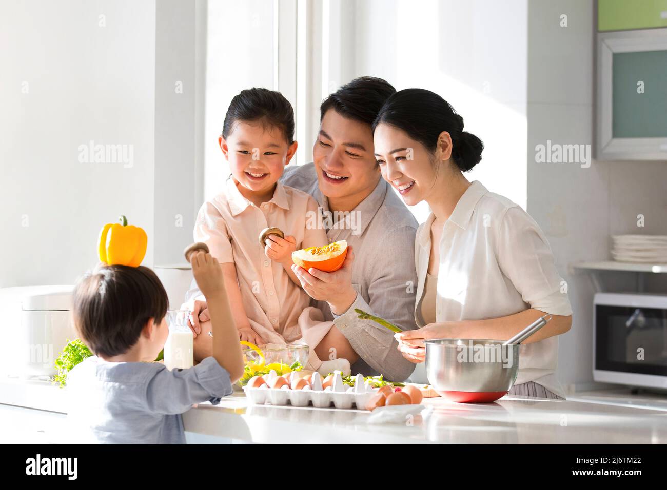 I giovani genitori giocano con i loro figli mentre cucinano, e il loro figlio malizioso usa un peperone sulla testa come cappello. - foto di scorta Foto Stock