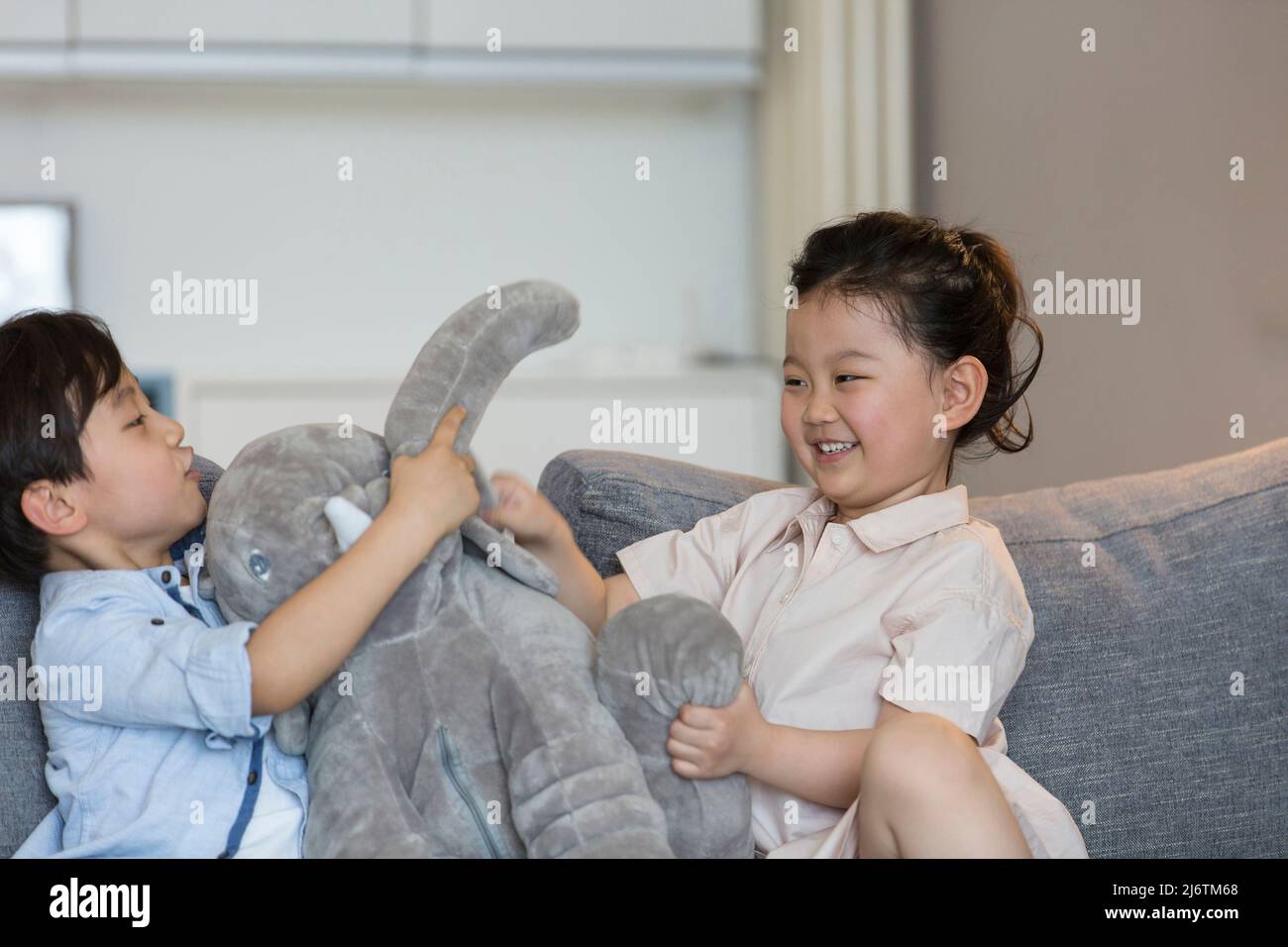 Una bambina e un ragazzino giocano felicemente con una bambola di elefante ripiena sul divano del soggiorno - foto di scorta Foto Stock