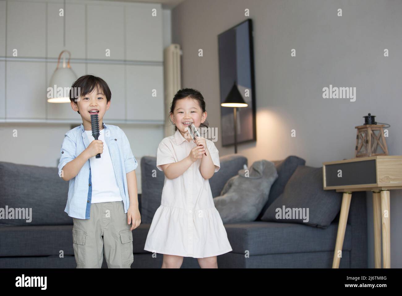 Una bambina e un ragazzino che cantano con un pettine come microfono nel soggiorno - foto di scorta Foto Stock
