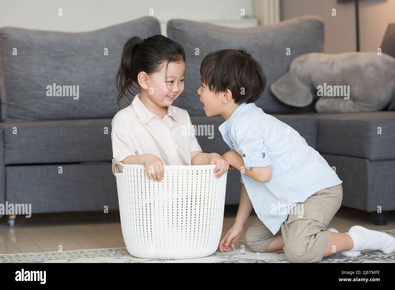 Dal divano del soggiorno, una bambina è pronta a sedersi nel cesto di vestiti e il ragazzino scherza con lei - foto di scorta Foto Stock