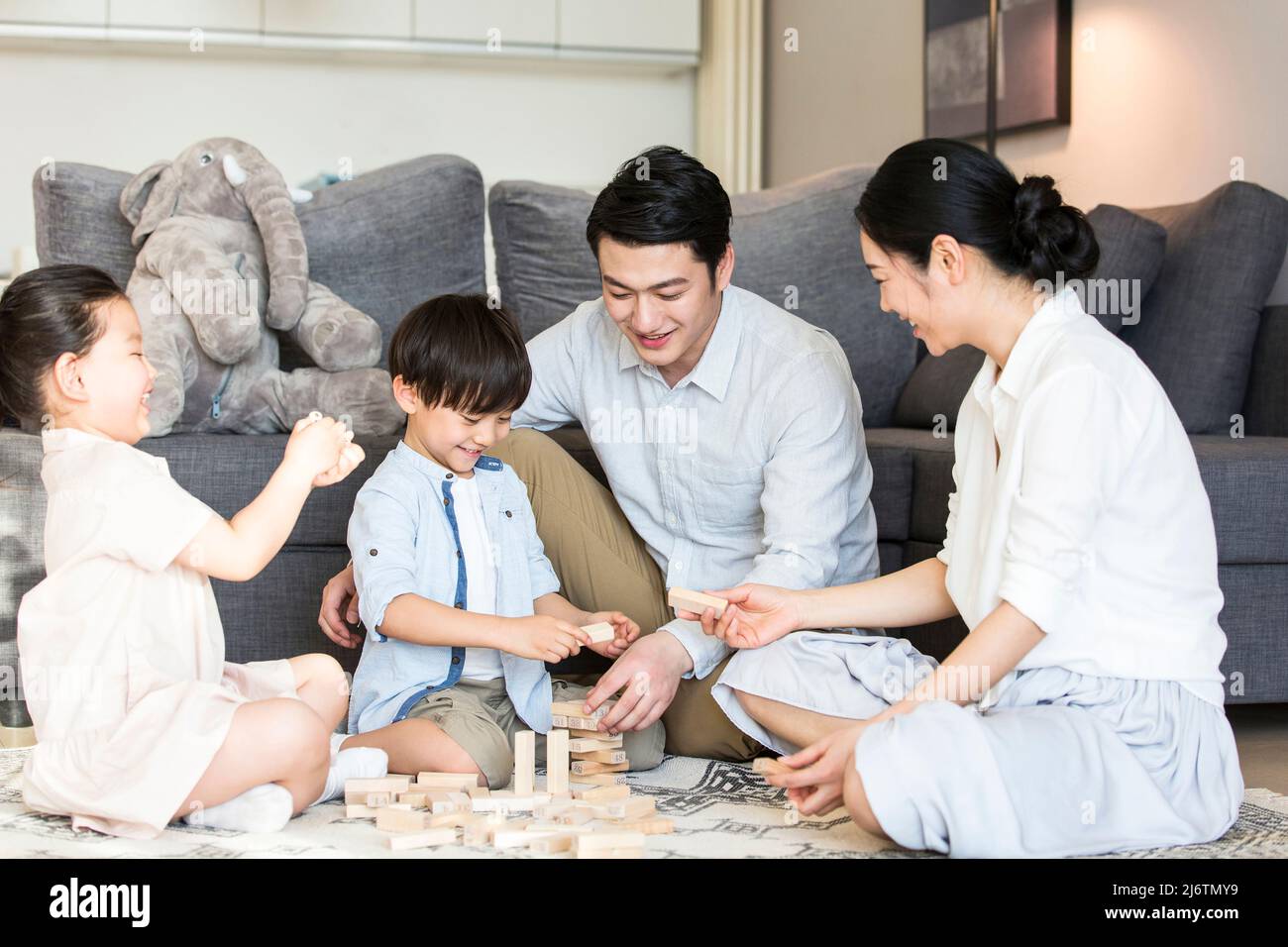 Un paio di genitori che accompagnano i loro due figli e figlie giocando con blocchi sul tappeto del soggiorno - foto di scorta Foto Stock